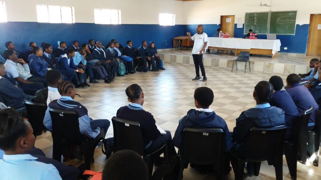 Facilitator addressing learners seated in a circle at a school hall session